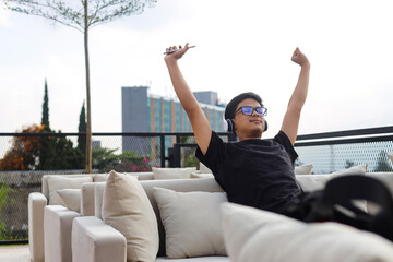 Freedom Asian young man relaxing and enjoying the time on rooftop couch while listening the music...