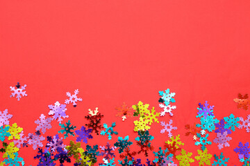 Colorful confetti in shape of snowflakes on red background, closeup