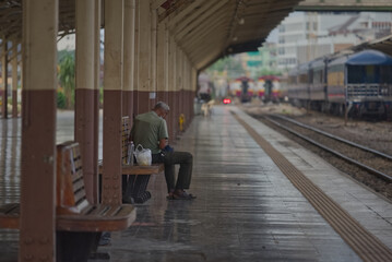 An old man is sitting on a wooden bench in a train platform