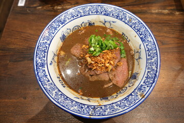 The close-up of Thai-style noodle soup with Wagyu beef from Japan on Thai- traditional bowl and wood table background.