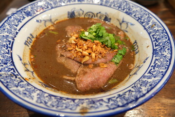 The close-up of Thai-style noodle soup with Wagyu beef from Japan on Thai- traditional bowl and wood table background.