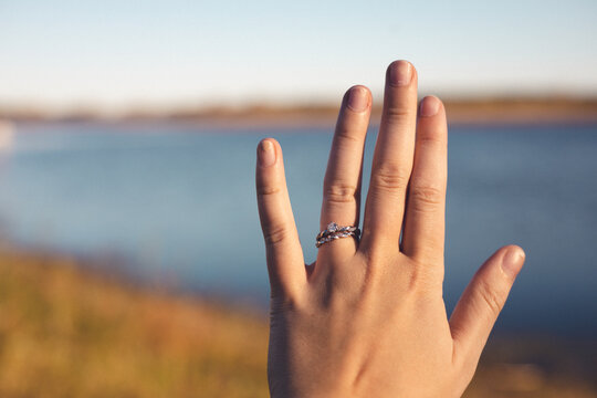 Symbol of love prominently displayed on young woman's hand. River and autumn grasses in the background. Sunny blue sky present in horizon. 