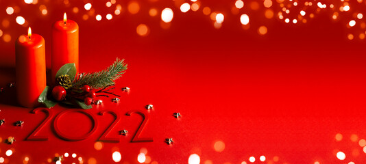 Wide banner congratulation happy new year and merry christmas in red. Two burning candles with a Christmas tree branch and the year 2022. Golden bokeh.