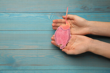 Woman holding paper cutout of small intestine on turquoise wooden background, top view. Space for...