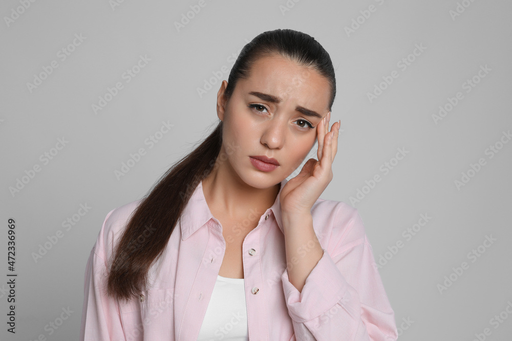 Sticker Young woman suffering from headache on light grey background