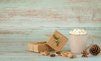 Beige mug with hot drink and marshmallows, craft gift boxes and orange's slices on blue wooden background