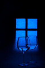 Still life with glass goblets with liquid against the background of a glowing window silhouette