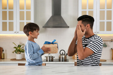 Man receiving gift for Father's Day from his son in kitchen