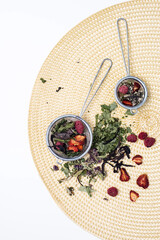 Fototapeta na wymiar Dried tea leaves and berries in tea strainer. Composition with organic, natural herbal tea and dry berry on wicker napkin.