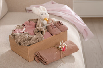 Fototapeta na wymiar Wooden crate with children's clothes, shoes, toy bunny and pacifier on sofa in room