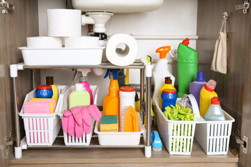 Open under sink cabinet with different cleaning supplies in kitchen