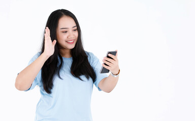 Studio shot of Asian chubby plump long black hair female model in blue casual t shirt and wristwatch smiling holding smartphone waving hand greeting say hi hello on video call on white background