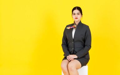 Portrait studio shot of Asian professional successful smart confident female flight attendant air hostess in formal uniform suit with scarf sitting smiling look at camera posing on yellow background