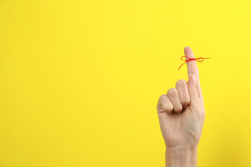 Woman showing index finger with tied red bow as reminder on yellow background, closeup. Space for text