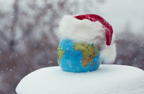The globe in the hat of Santa Claus, in winter in the snow