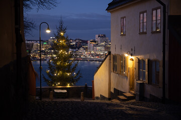 Decorated Christmas tree with a lamppost on the edge of the hill with night city panorama and old...