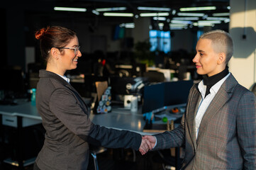 Two young business women shake hands at work. The office staff made a deal