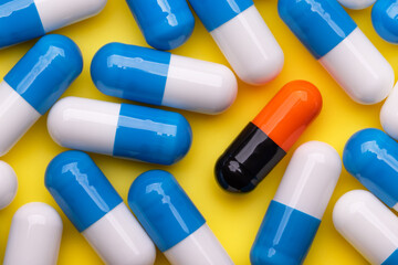 Blue and white drug capsules and one black and orange on a yellow background. Pharmacy.