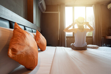 Tourist woman sitting on bed in hotel bedroom after check-in and looking to beautiful view outside...