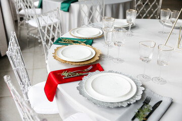 Beautiful festive table setting with napkins of different colors. A luxurious dining set with cutlery, napkin, dishes and covered with a tablecloth in the restaurant. Gold plates and crystal glasses. 