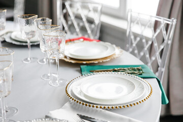 Beautiful festive table setting with napkins of different colors. A luxurious dining set with cutlery, napkin, dishes and covered with a tablecloth in the restaurant. Gold plates and crystal glasses. 