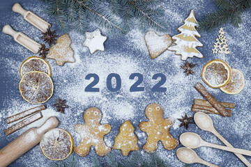 Happy New Year 2022 written in flour. Christmas bakery background with ingredients for cooking. They ate twigs, gingerbread, little men. Top view of flour, spices, toys