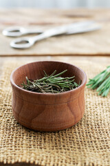 Dry rosemary in a wooden bowl with scissors on the table. Rustic style. The dry spice is added to meat, salads, soups or drinks. Ingredient for the bouquet Garni, Provencal herbs and Italian herbs.