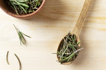 Dry rosemary in a wooden bowl with a spoon and a few sprigs on a wooden table. Rustic style. The...