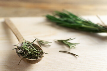 A spoon with dry rosemary and a bunch of fresh twigs lies on a wooden table. Rustic style. Ingredient for the bouquet Garni, Provencal herbs and Italian herbs. Copy space. Selective focus.