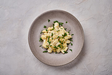 Flat lay traditional Alpine dish gnocchi, prepared with potato and whole grain flour dough with cream sauce and parsley on gray plate