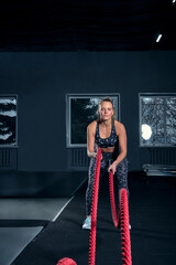 Vertical full length shot of an athletic fitness woman doing functional training exercise with battle ropes at the gym Cross Fit cross training strength endurance energy power concept