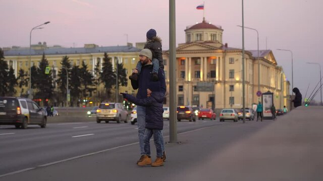 Saint-petersburg.Father walking with sons along street of Saint-Petersburg near road with car traffic. Little boy sitting on da shoulders