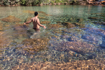 young man standing in flowing river clear water at morning from flat angle
