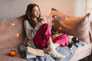 Young woman with cat drinking warm coffee at home