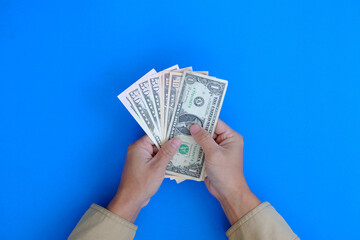 Hand holding a bank note with the concept of money on a blue background represents finance and banking.