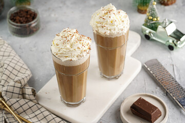 Two tall glasses with cold coffee drink frappe - iced cappuccino with whipped cream on a marble board and christmas ornaments and decoration