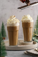 Grating chocolate over two tall glasses with cold coffee drink frappe - iced cappuccino with...