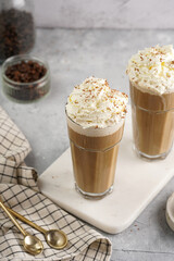 Two tall glasses with cold coffee drink frappe - iced cappuccino with whipped cream on a marble board