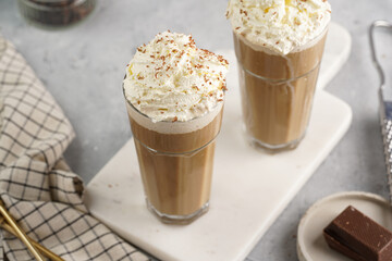 Two tall glasses with cold coffee drink frappe - iced cappuccino with whipped cream on a marble board
