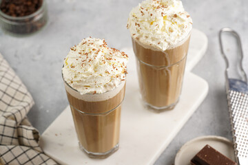 Two tall glasses with cold coffee drink frappe - iced cappuccino with whipped cream on a marble board