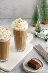 Two tall glasses with cold coffee drink frappe - iced cappuccino with whipped cream on a marble board and christmas ornaments and decoration