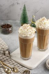 Two tall glasses with cold coffee drink frappe - iced cappuccino with whipped cream on a marble board and christmas ornaments and decoration