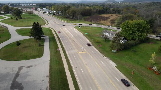 Wide highway in rural western Wisconsin. Forest and mountains seen in background with blue sky. Sidewalk running along one side. 