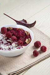 Close-up of a bowl of smoothies made of apples, beets and raspberries with walnuts and coconut shavings.