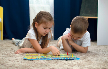 Portrait of two children lying on the floor and playing the board game walker in the nursery. A board game and the concept of children's leisure. Selective focus