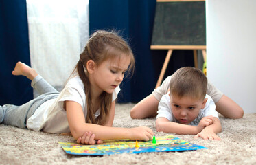 Portrait of two children lying on the floor and playing the board game walker in the nursery. A...
