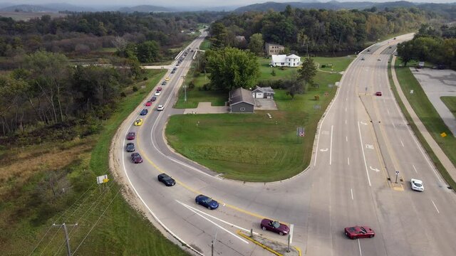 Corvette car parade through rural roads in Wisconsin. Cars turning onto highway. Residential home and garage on corner. Multiple directional signs present. 