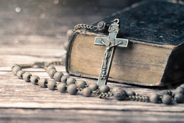 Detail studio shot of very old, vintage Holy Bible with lots of ornaments on the cover and yellow pages and old rosary on vintage wooden desk Christianity concept. Time of prayer