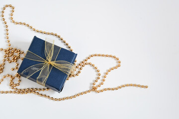 Christmas gift box wrap with blue navy paper and golden ribbon on golden necklace on white background with space for text. Handmade objects , Christmas holiday concept.