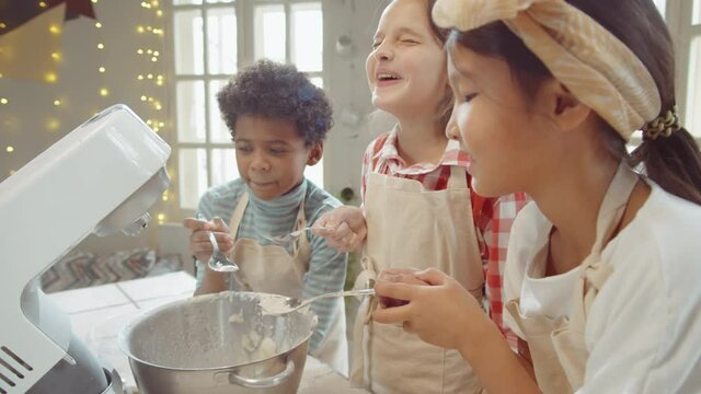 Little diverse children blowing flour out of spoons into mixer bowl and then laughing on cooking masterclass